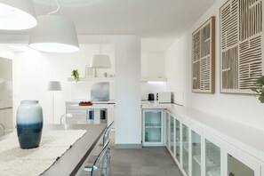 A modern kitchen with white cabinetry, a central island, pendant lighting, and a decorative wall panel. - VILLA MELOGRANO - A blend of discreet elegance and total comfort, only 500 meters from Sardinia’s most stunning waters (Castiadas)
