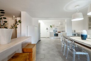A modern kitchen with a central island, clear chairs, and a white countertop. - VILLA MELOGRANO - A blend of discreet elegance and total comfort, only 500 meters from Sardinia’s most stunning waters (Castiadas)
