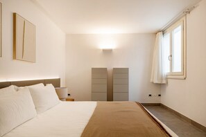 A hotel room with a large bed, a nightstand, a wall-mounted light, and a window with curtains. - VILLA MELOGRANO - A blend of discreet elegance and total comfort, only 500 meters from Sardinia’s most stunning waters (Castiadas)