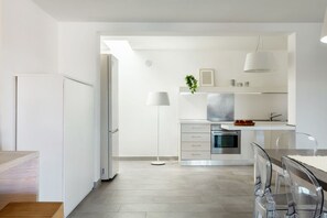 A modern kitchen with white cabinetry, a built-in oven, and a dining area with transparent chairs. - VILLA MELOGRANO - A blend of discreet elegance and total comfort, only 500 meters from Sardinia’s most stunning waters (Castiadas)