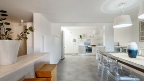 Una cocina moderna con una isla central, sillas transparentes y encimera blanca.