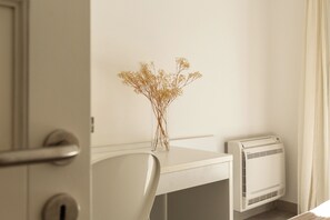A white desk with a clear vase containing dried flowers, a white chair, and a white air conditioning unit. - VILLA MELOGRANO - A blend of discreet elegance and total comfort, only 500 meters from Sardinia’s most stunning waters (Castiadas)