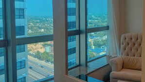 A room with large windows offering a city view, a tufted armchair, and a glass table.