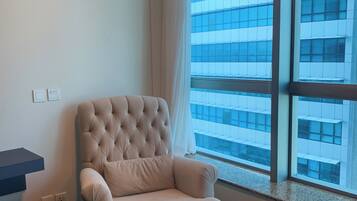 A modern room with a large window, a tufted armchair, a matching ottoman, and a dark wooden floor.