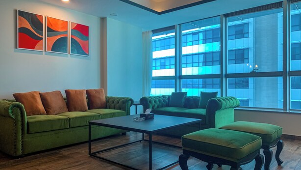 A modern living room with a green sofa set, a coffee table, and a large window with a view of a building.