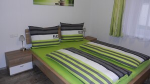 Een netjes opgemaakt slaapkamer met een bed, kussens, een nachtkastje, een lamp en een aan de muur hangend schilderij.