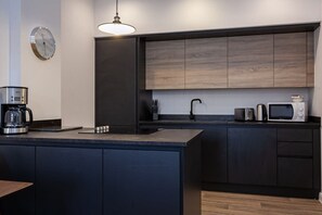 A modern kitchen with dark cabinetry, a built-in microwave, and a coffee maker on the counter. - Chic 1BR Bolton Apt near Manchester Rail (Bolton)