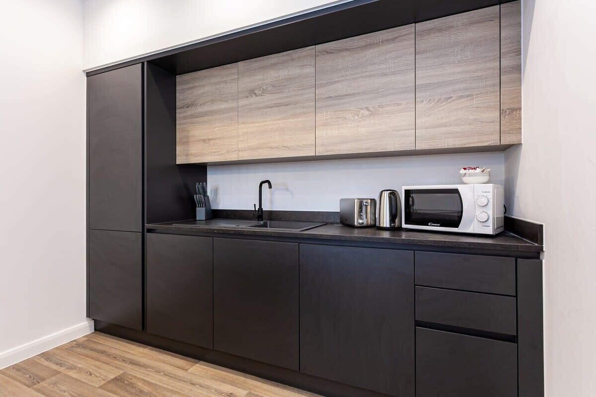 Une cuisine moderne avec des meubles de couleur sombre, un plan de travail en bois, un évier, un grille-pain et un four à micro-ondes.