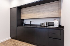 A modern kitchen with dark cabinetry, a wooden countertop, a sink, a toaster, and a microwave.