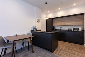 A modern kitchen with dark cabinetry, a central island, and a dining area with a table and chairs.