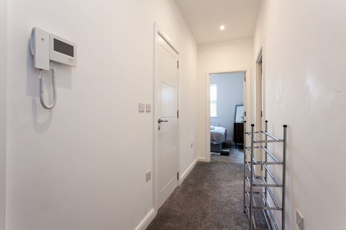 A hallway with a white door, a wall-mounted intercom, and a metal rack.