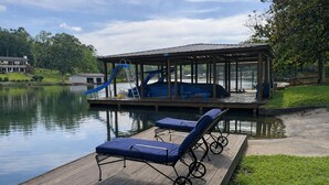 Un muelle de madera con sillones de descanso, un área techada con un tobogán y vista al lago.