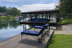 Eine Holzterrasse mit Liegestühlen, einem überdachten Bereich mit Rutsche und Blick auf einen See.