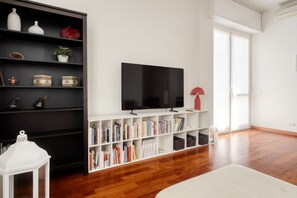 A living room with a flat-screen TV, bookshelves, a white floor lamp, and a white table with a lantern. - Hostmate - Milano - Messina - ChinaTown (Milano)