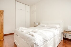 A bedroom with a bed, white wardrobe, wooden floor, and a small table with a lamp. - Hostmate - Milano - Messina - ChinaTown (Milano)