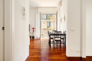 A hallway leading to a dining area with a wooden floor, a table with chairs, a telephone on the wall, and a window with a view of the outside. - Hostmate - Milano - Messina - ChinaTown (Milano)