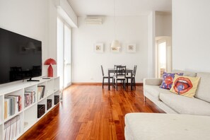 A living room with a television, bookshelves, a dining table, and a sofa. - Hostmate - Milano - Messina - ChinaTown (Milano)