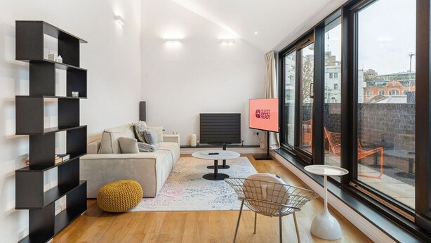 A modern living room with a sofa, coffee table, and a TV screen displaying "GUEST READY". - Stylish Hoxton Duplex – Perfect for Couples & Small Groups (London)