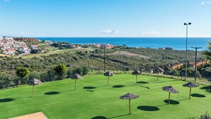 En golfbana med parasoller av halmtak, fri utsikt över havet och en stad i bakgrunden.