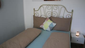 Una cama con cabecera de metal, dos almohadas, una almohada colorida y una mesita de noche con una vela encendida.