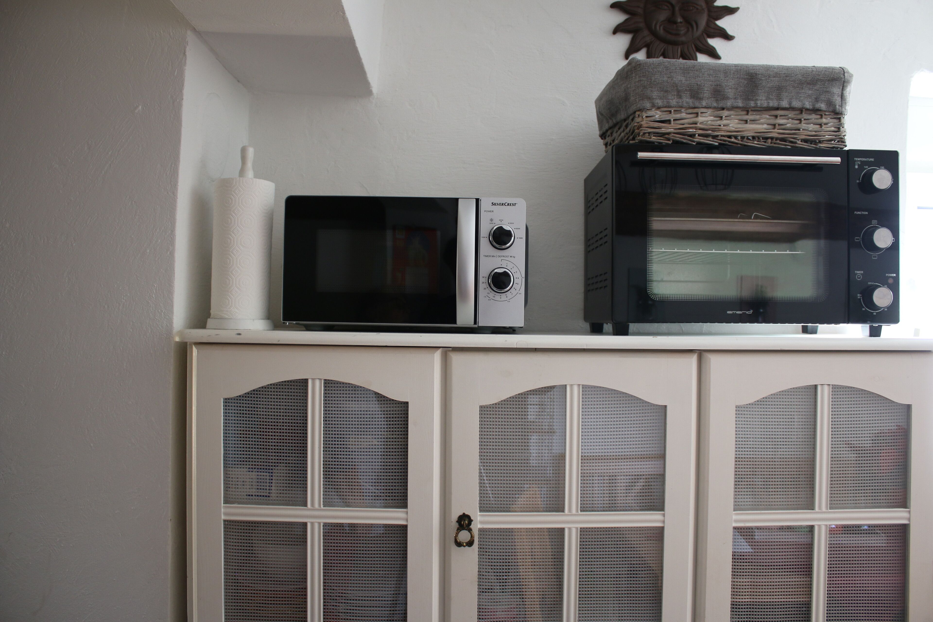 Un microondas y un horno tostador sobre un mueble con una cesta tejida encima.