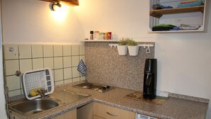 A small kitchen with a sink, stove, and coffee maker. There are cabinets, a shelf with spices, and a window above the sink. - Vacation cottage Ewald (Enkirch)