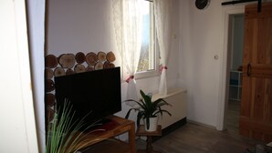 A living room with a flat-screen TV, a wooden coffee table, a potted plant, a window with curtains, and a wall-mounted clock. - Vacation cottage Ewald (Enkirch)