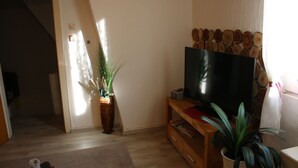 A living room with a wooden entertainment unit, a flat-screen TV, a potted plant, and a staircase leading to another room. - Vacation cottage Ewald (Enkirch)