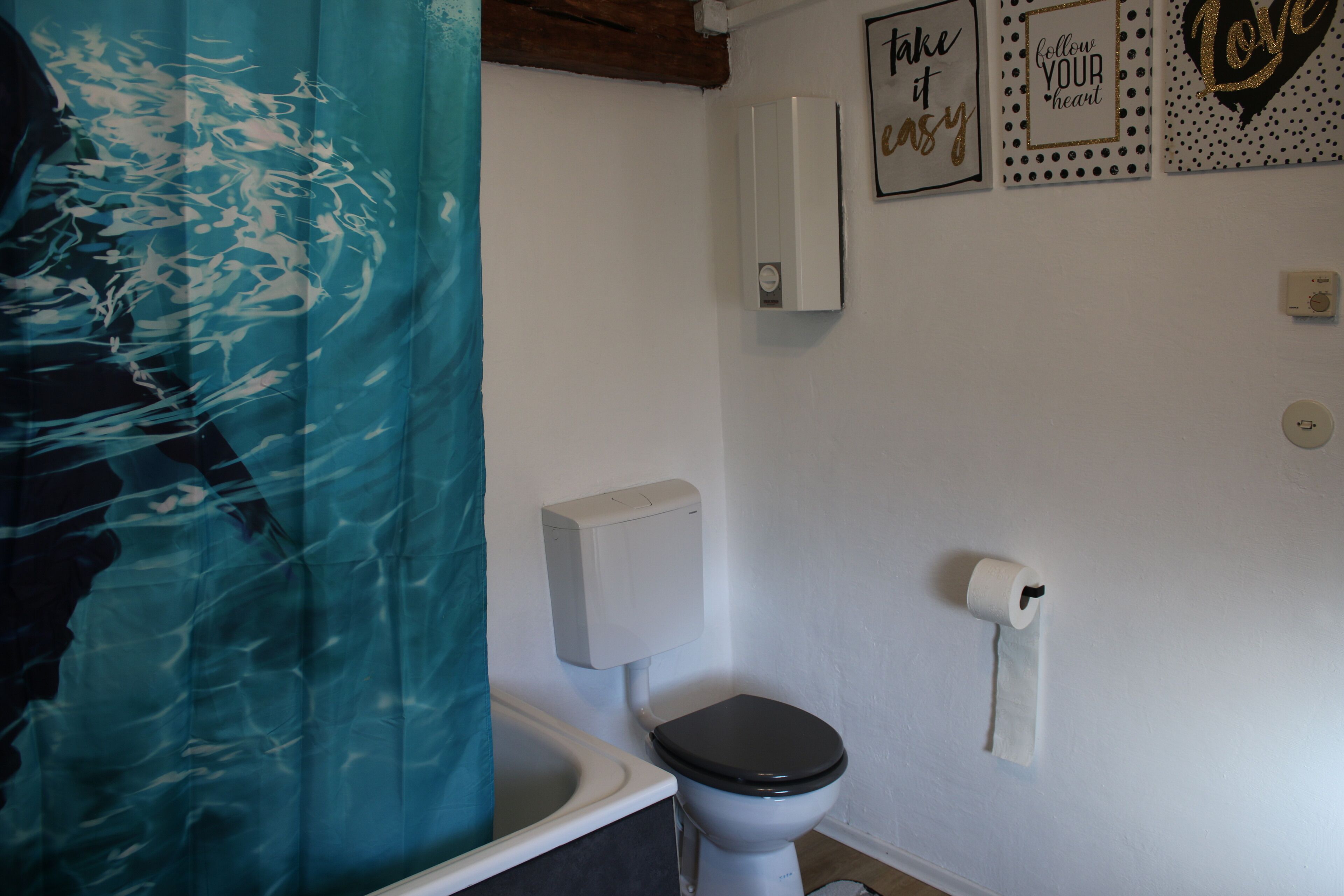 A bathroom with a toilet, a roll of toilet paper, and a wall-mounted air freshener.