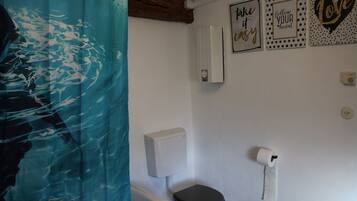 A bathroom with a toilet, a roll of toilet paper, and a wall-mounted air freshener.