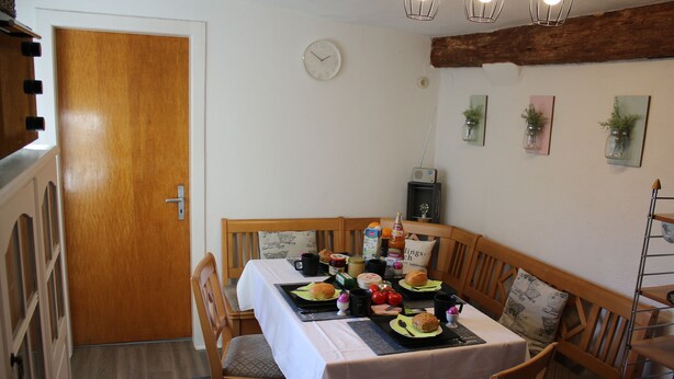 A dining area with a wooden table set for two, a clock on the wall, and a rustic ceiling. - Vacation cottage Ewald (Enkirch)