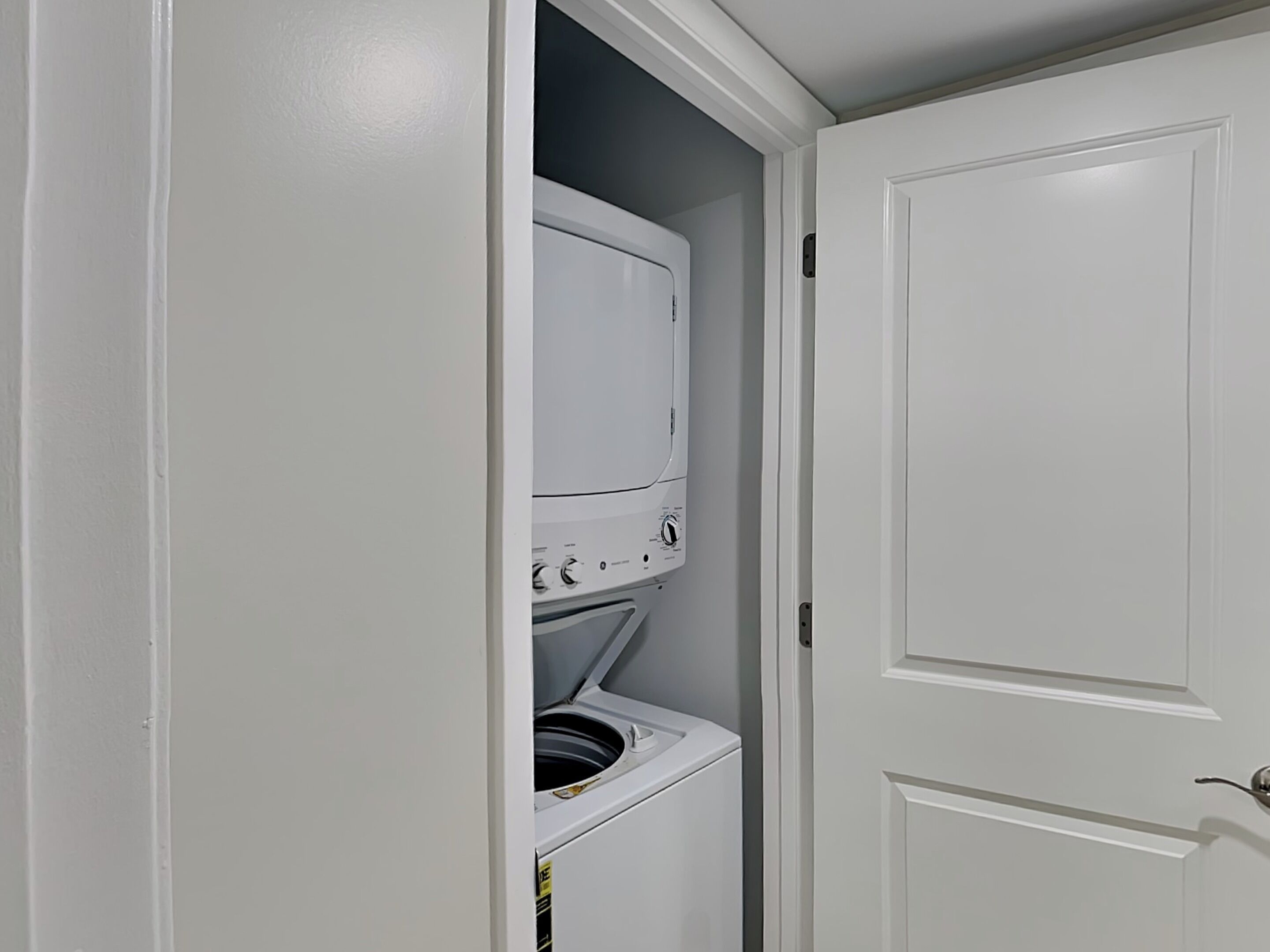 A laundry room with a stacked washer and dryer, a white door, and a small window.