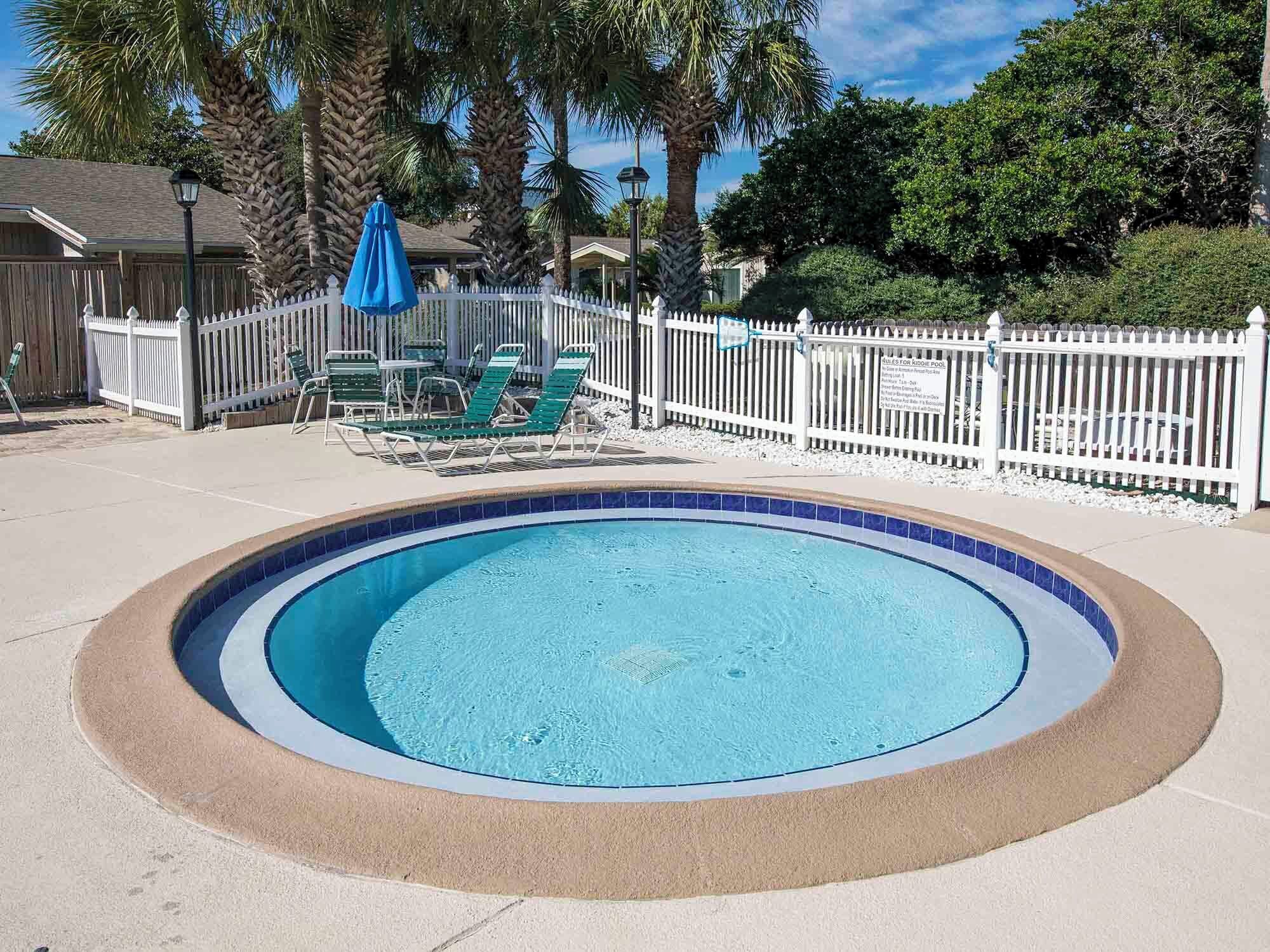Una piscina circular con cerca blanca y sillas de descanso verdes.