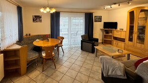 A living room with a dining table, sofa, TV, and wooden cabinets. - Fewo Eichhölzle 1, 90 sqm, 2 Bedrooms, Max. 4 Guests (Münsingen)