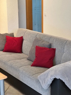 Un sofá gris con dos almohadas rojas y una manta gris.