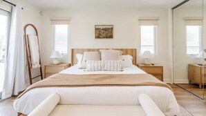 Ein Schlafzimmer mit einem großen Bett, zwei Nachttischen, einem Spiegel und einem Fenster mit Vorhängen.