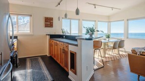 A modern kitchen with wooden cabinets, a central island, and large windows offering ocean views. - Serene Escape at Windansea: Oceanview 2-Bedroom (San Diego)
