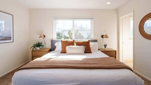 A bedroom with a large bed, two bedside tables, a window, and a view of the outdoors. - Serene Escape at Windansea: Oceanview 2-Bedroom (San Diego)