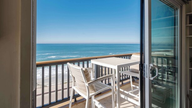 A balcony with a view of the ocean, a white table, and a white chair. - Serene Escape at Windansea: Oceanview 2-Bedroom (San Diego)