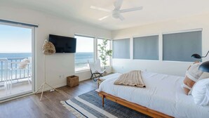 A bedroom with a bed, a ceiling fan, a TV, a chair, and a view of the ocean. - Beachfront Bliss: Oceanview Haven at Windansea (San Diego)