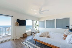 Un dormitorio con cama, ventilador de techo, televisor, una silla y vista al océano.