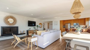 A modern living room with a white sofa, wooden floor, and a dining area with a table and chairs. - Beachfront Bliss: Oceanview Haven at Windansea (San Diego)