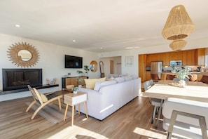 Una sala de estar moderna con un sofá blanco, piso de madera y un comedor con mesa y sillas.