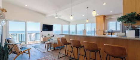 A modern kitchen with a bar area, large windows, and a view of the ocean.
