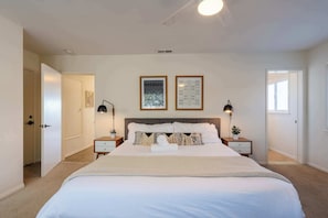 A bedroom with a large bed, two bedside tables, a ceiling fan, and framed pictures on the wall. - Windansea Bliss: Relax in This Beachfront Haven (San Diego)