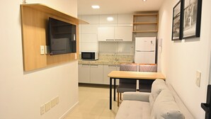 Cocina compacta con microondas, refrigerador y zona de comedor con mesa y sofá.