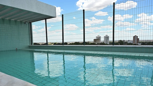 Una piscina interior con agua cristalina y azul, rodeada por un muro de azulejos y una valla de metal.