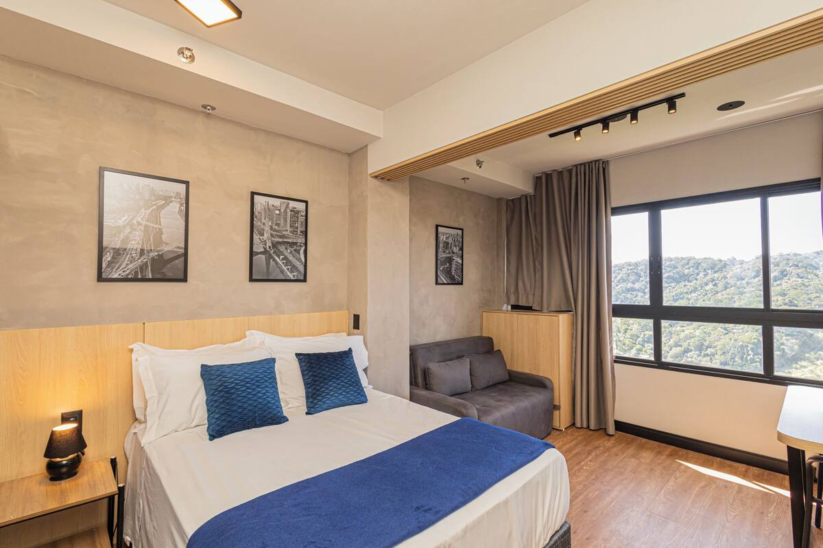 A hotel room with a bed, a desk, a chair, and a large window with a view.