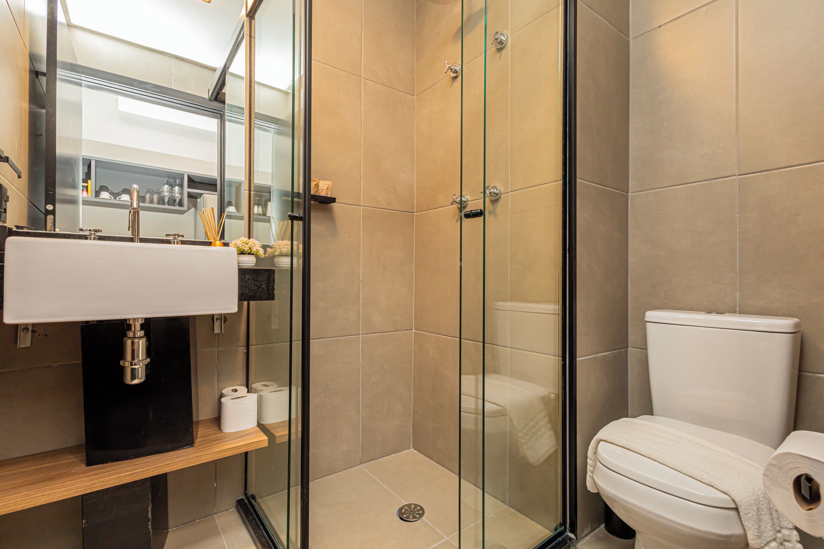 Un baño moderno con ducha envuelta en vidrio, un inodoro blanco y un lavamanos con mueble negro.