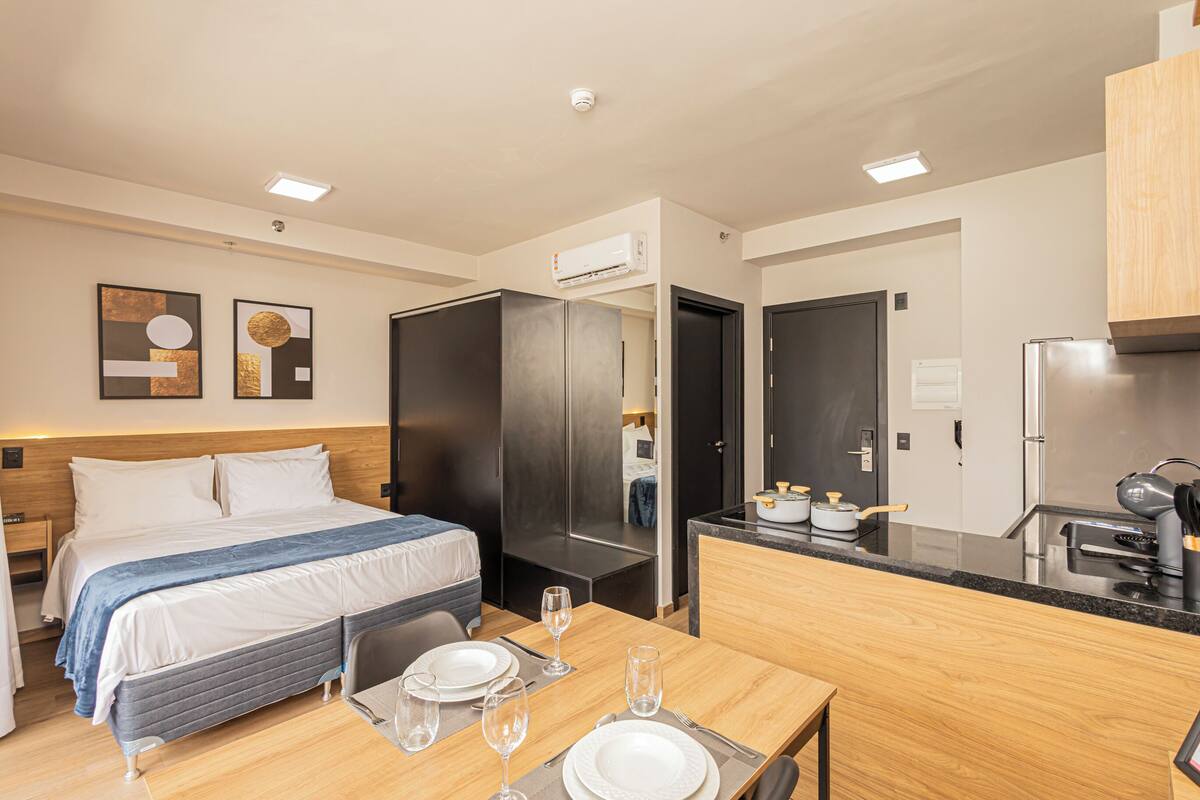 A modern hotel room with a bed, bedside table, and a small kitchenette.